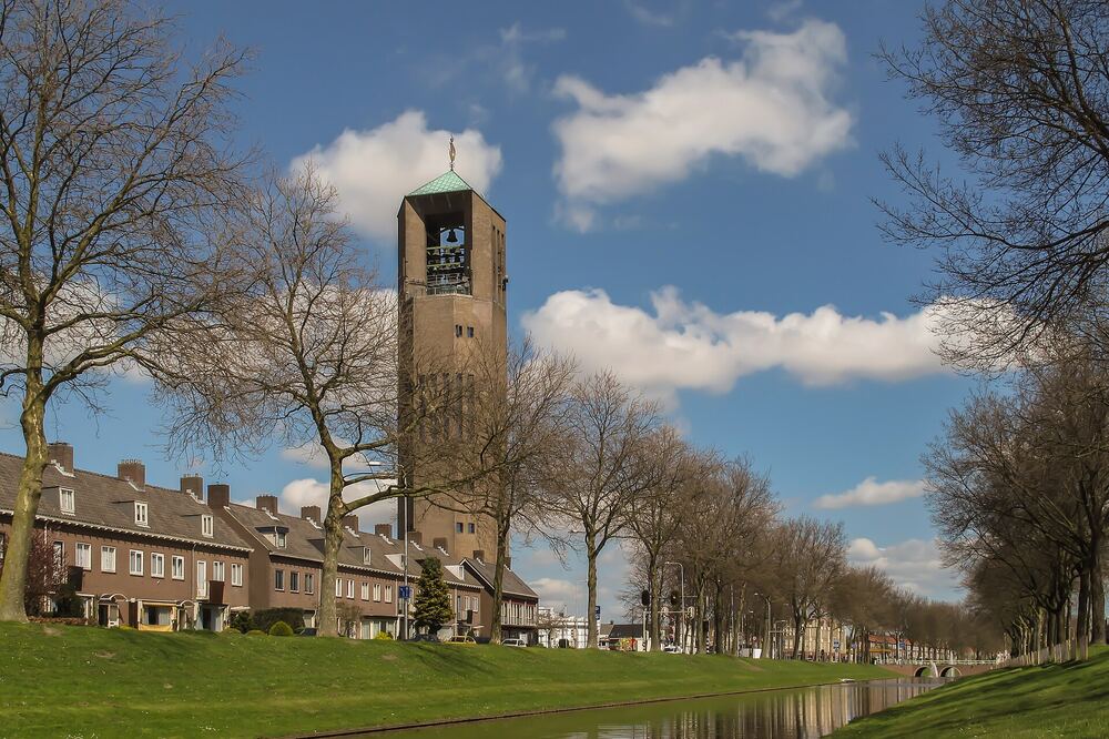 De Poldertoren van Emmeloord boven de daken, gezien vanaf een lommerrijke straat langs het water